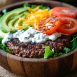 A vibrant burger bowl with beef patties, fresh vegetables, and cheese in a wooden bowl.